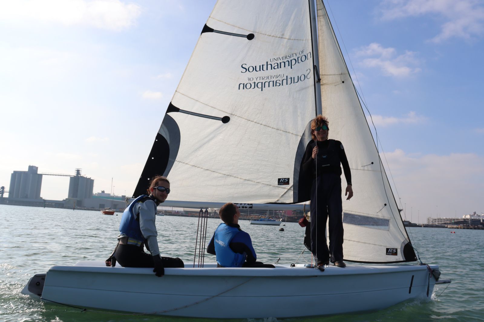 Trois étudiants naviguent sur un dériveur aux couleurs de l’Université de Southampton, dans le port de Southampton.